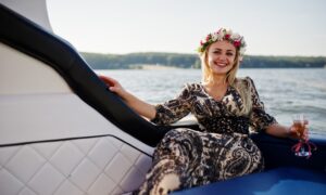 Blonde girl in wreath sitting on yacht at hen party with champagne.