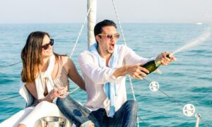 Young couple in love on sailing boat cheering with champagne wine bottle